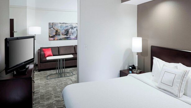 Ein Hotelzimmer mit einem großen Bett, einem Flachbildfernseher, einer Couch, einem kleinen Tisch und einem Gemälde an der Wand.