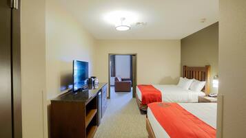 A hotel room with a bed, a desk with a television, a chair, and a nightstand with a lamp.