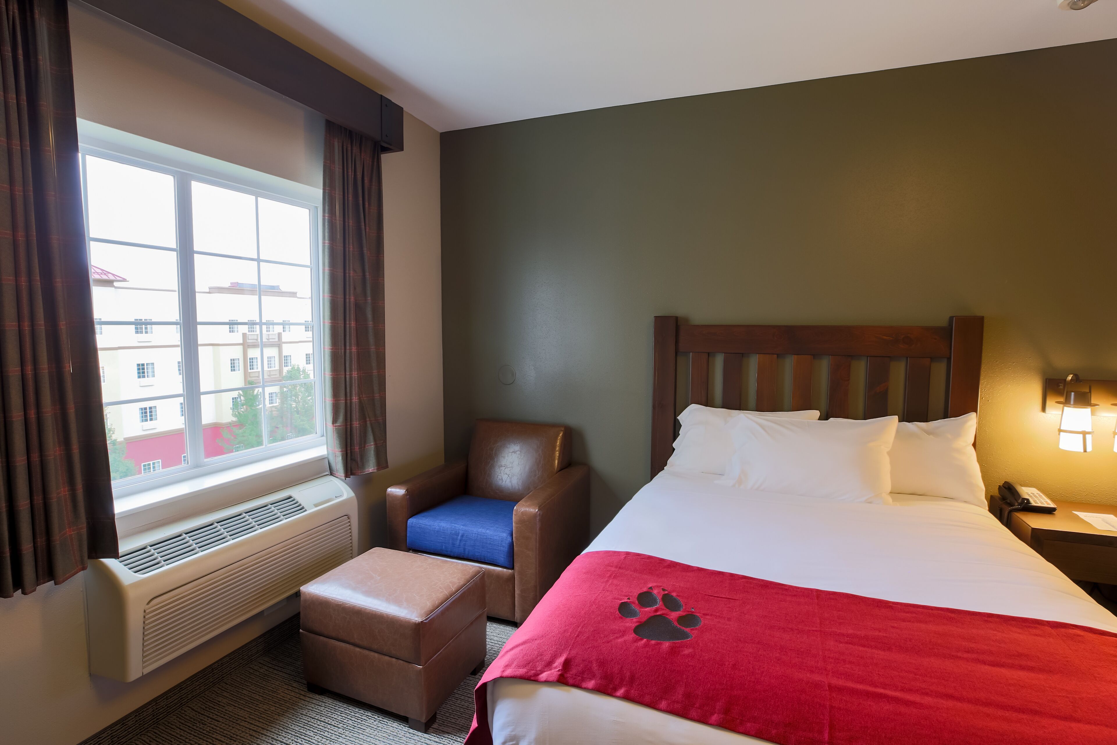 Een hotelkamer met een bed, een stoel, een verwarming en een raam met gordijnen.