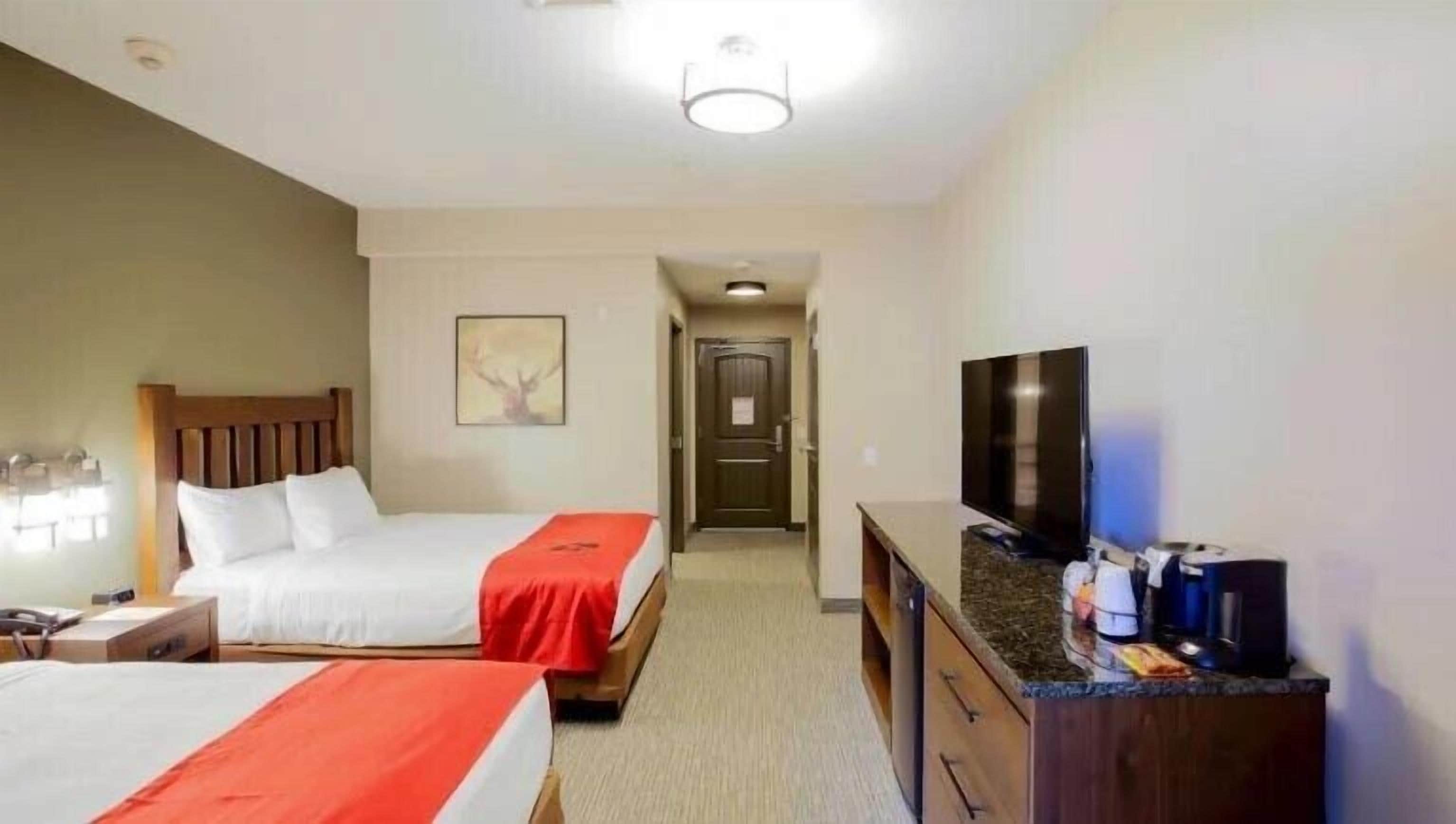 A hotel room with two beds, a TV, a dresser, and a hallway leading to another room.