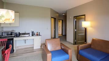 Une chambre d’hôtel de taille réduite, équipée d’une kitchenette, d’un canapé, d’un fauteuil et d’une lampe.