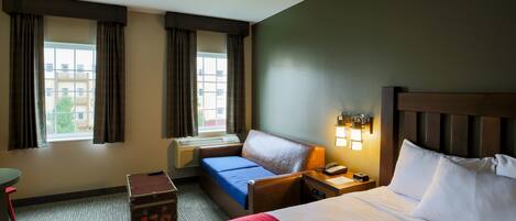 Een hotelkamer met een bed, bureau, stoel, koffer en raam met gordijnen.