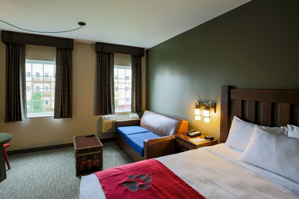 A hotel room with a bed, a desk, a chair, a suitcase, and a window with curtains. - Great Wolf Lodge Illinois (Gurnee)