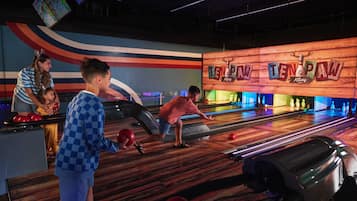Une salle de bowling avec plusieurs pistes, un panneau en bois indiquant l’entrée, et un mur coloré orné d’un motif ondulé.