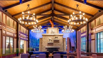 A lodge interior with a stone fireplace, wooden beams, and multiple seating areas.