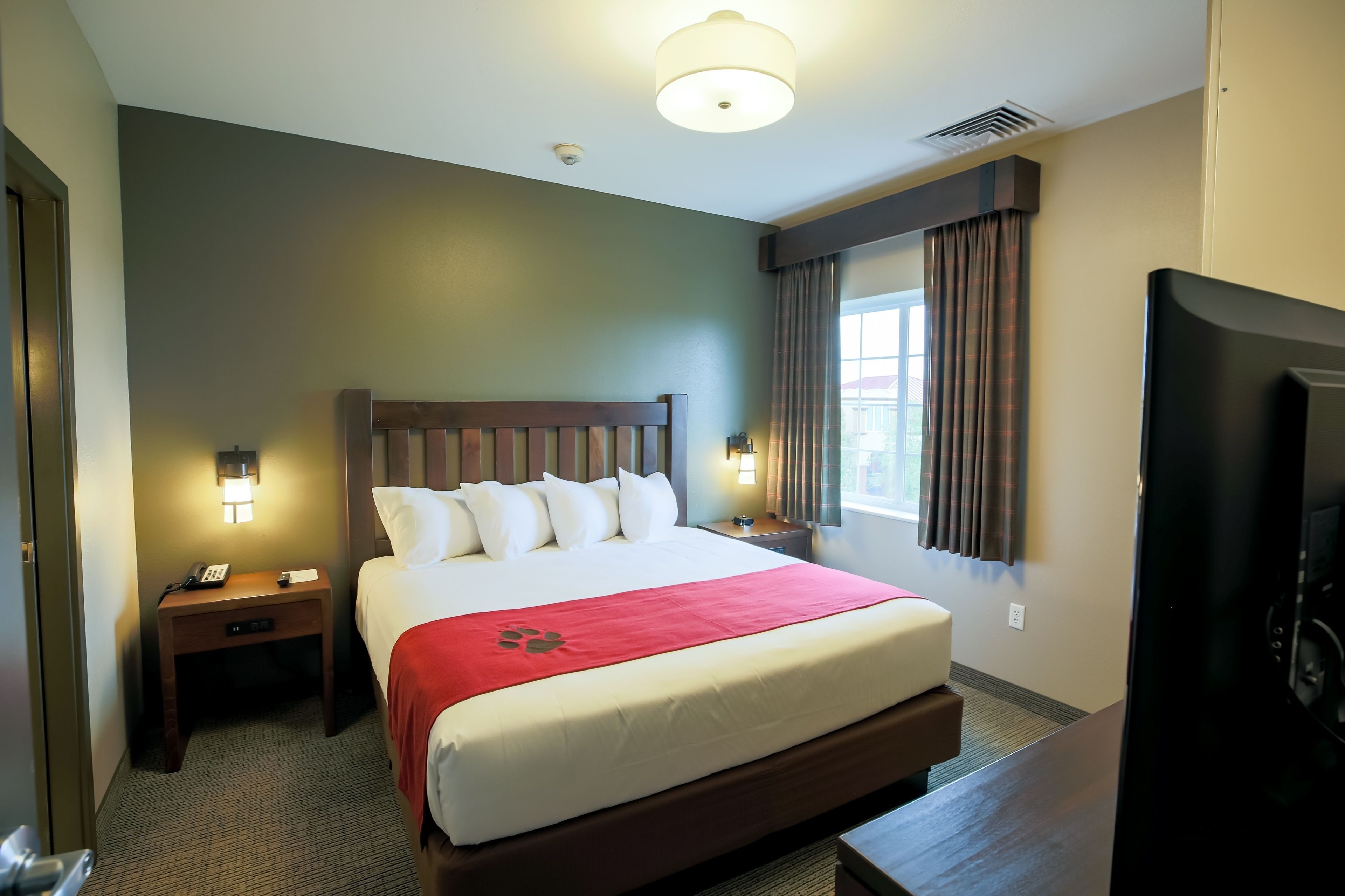 A hotel room with a large bed, two bedside tables with lamps, a TV, and a window with curtains.