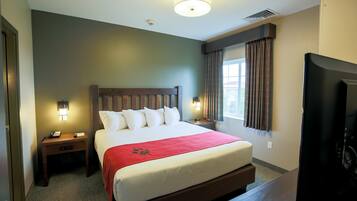 A hotel room with a large bed, two bedside tables with lamps, a TV, and a window with curtains.