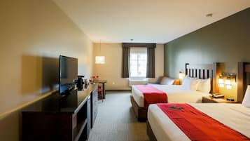 Une chambre d’hôtel équipée d’une télévision, d’un bureau, de deux lits, d’une fenêtre avec des rideaux et d’une table de chevet avec une lampe.