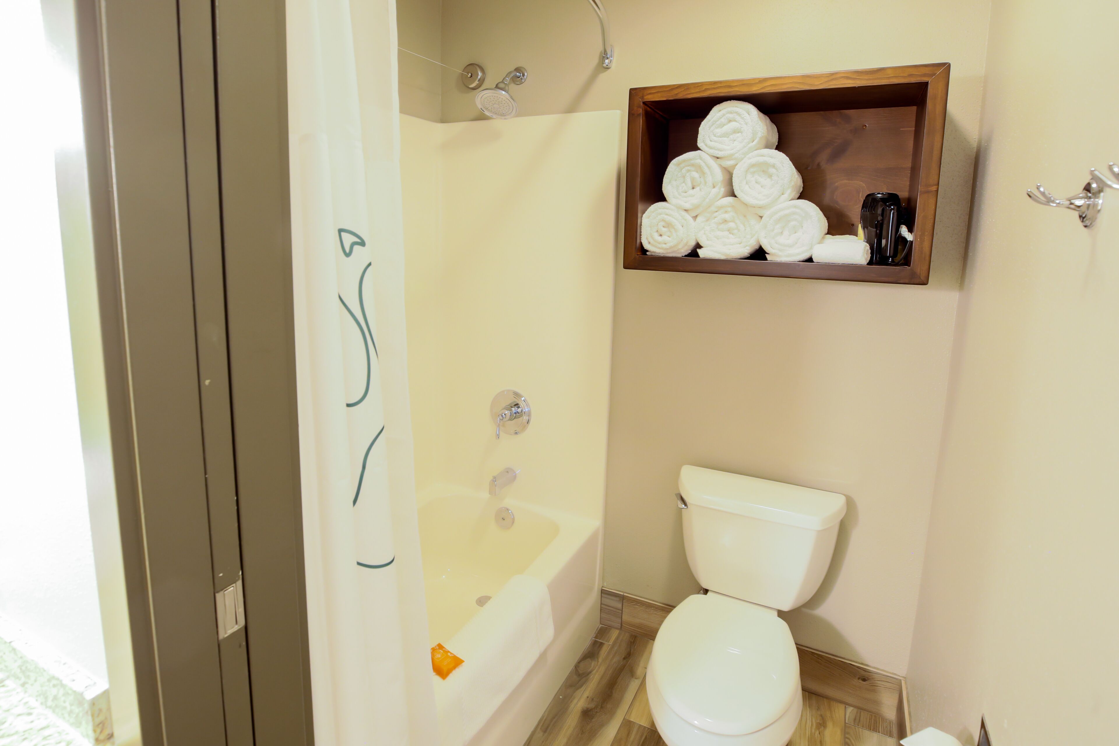 A bathroom with a bathtub, toilet, and a wooden shelf with towels.