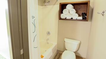 A bathroom with a bathtub, toilet, and a wooden shelf with towels.