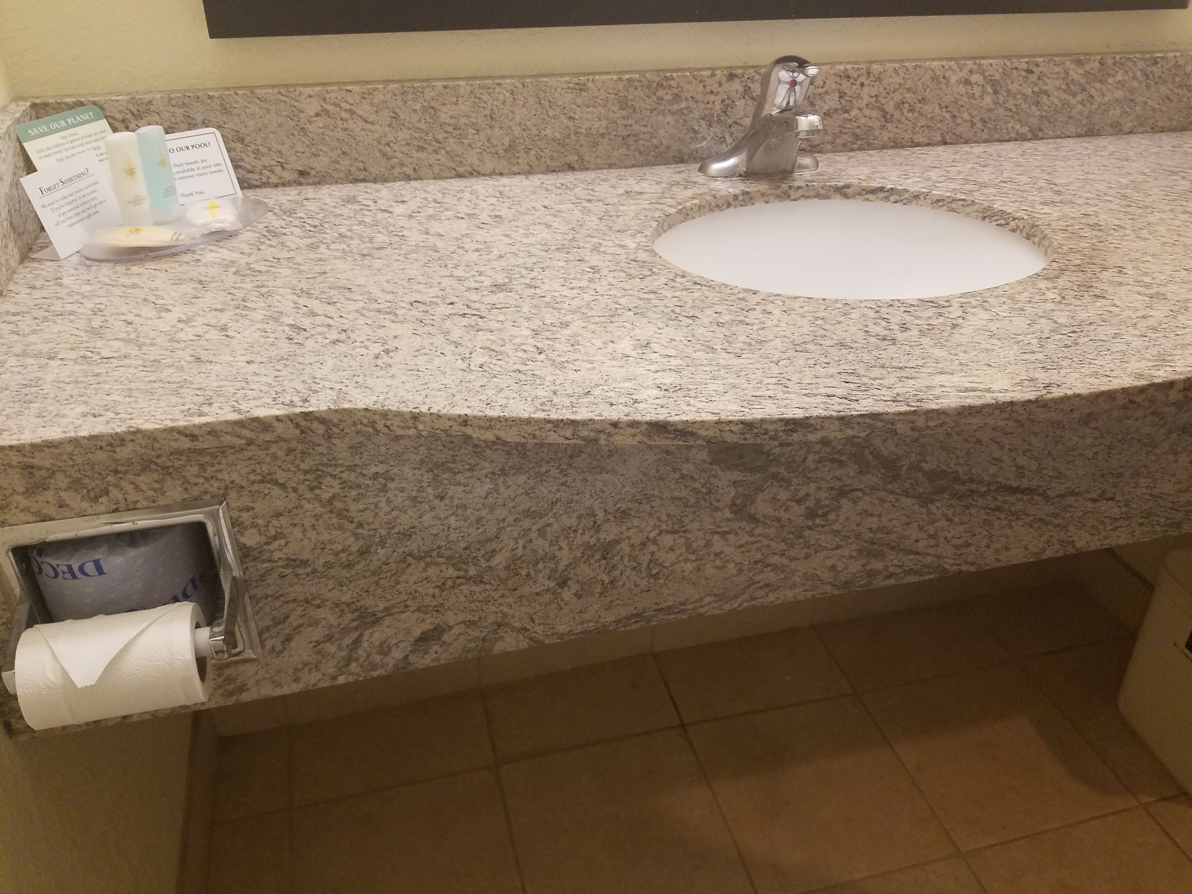 Een badkamer met een granieten aanrecht, een wastafel en een papieren handdoekdispenser.