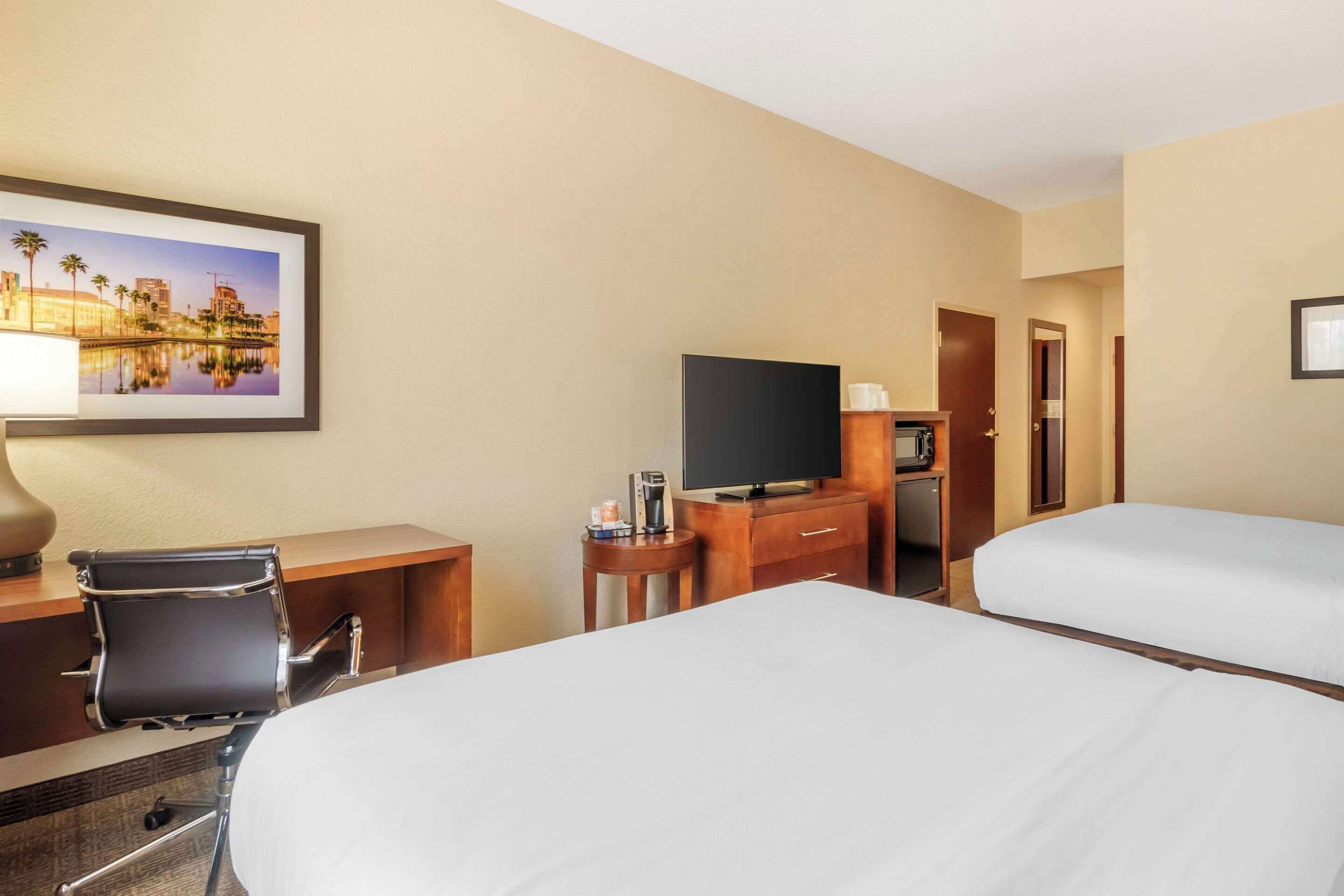 A hotel room with two beds, a desk with a chair, a television, and a coffee maker.