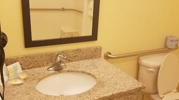 Un baño con lavamanos de encimera de granito, un espejo, un inodoro y un dispensador de toallas.