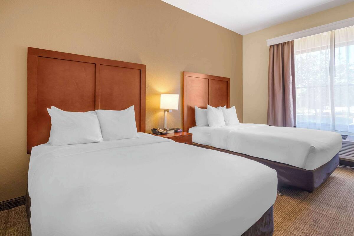 Ein Hotelzimmer mit zwei Betten, einem Nachttisch mit Lampe und einem Fenster mit Vorhängen.