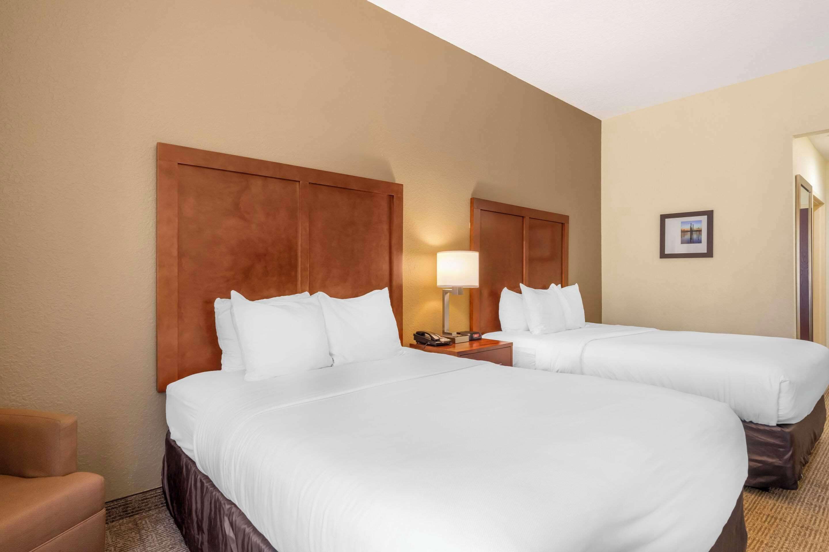 Une chambre d’hôtel avec deux lits simples, une table de chevet avec une lampe, une chaise et un tableau encadré au mur.