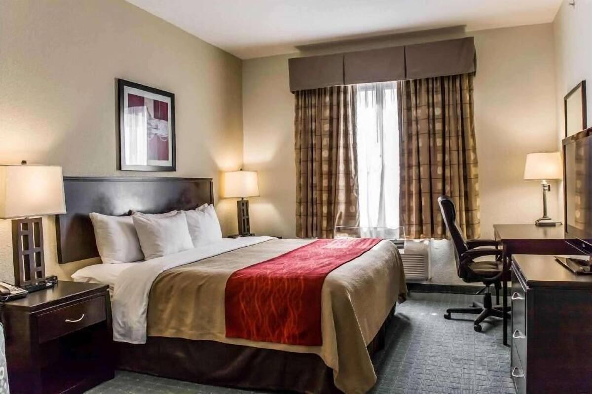 Ein Hotelzimmer mit Bett, Nachttischen, Schreibtisch, Stuhl, Fernseher und einem Fenster mit Vorhängen.