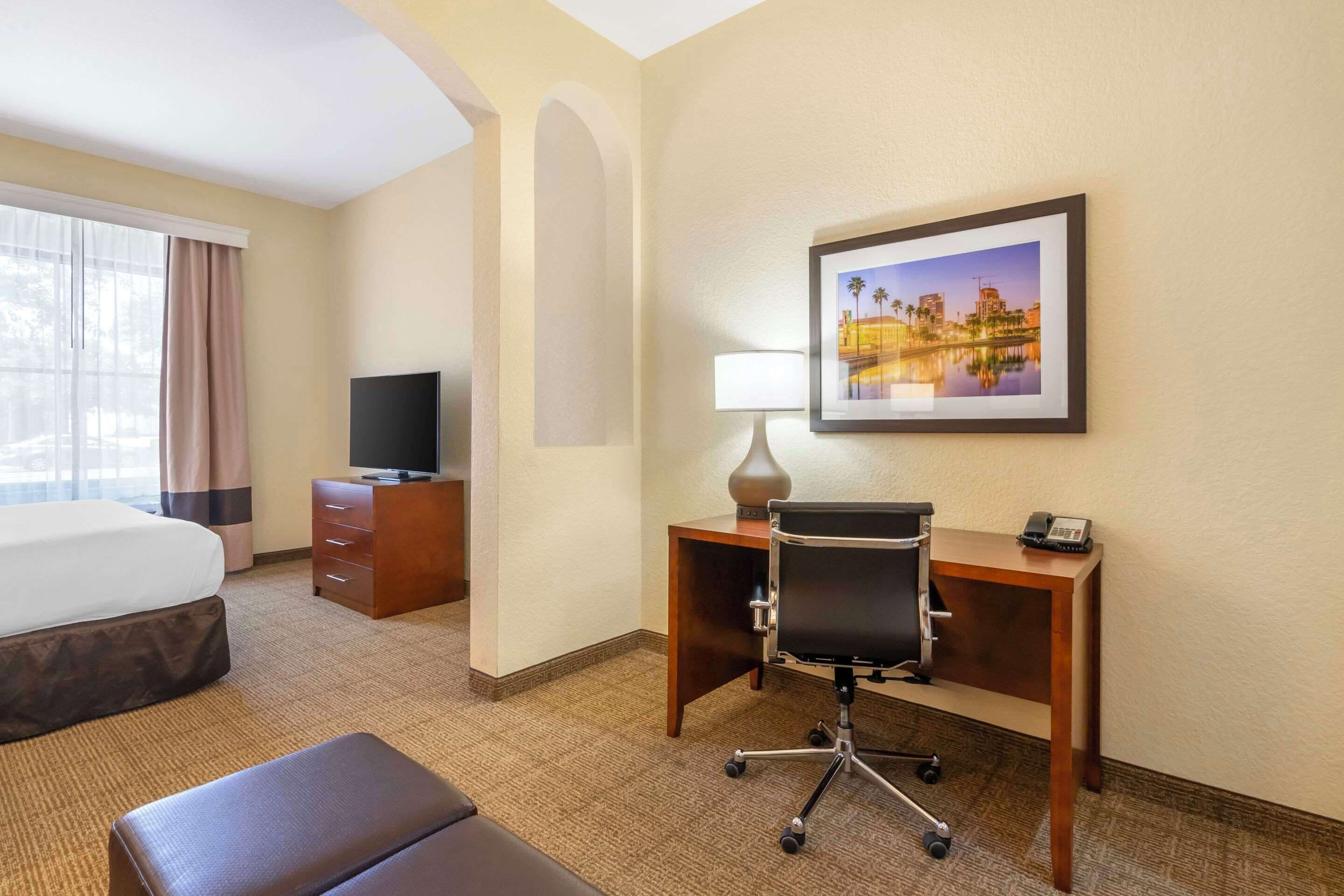 A hotel room with a bed, a desk with a chair, a television, a lamp, and a framed picture on the wall.