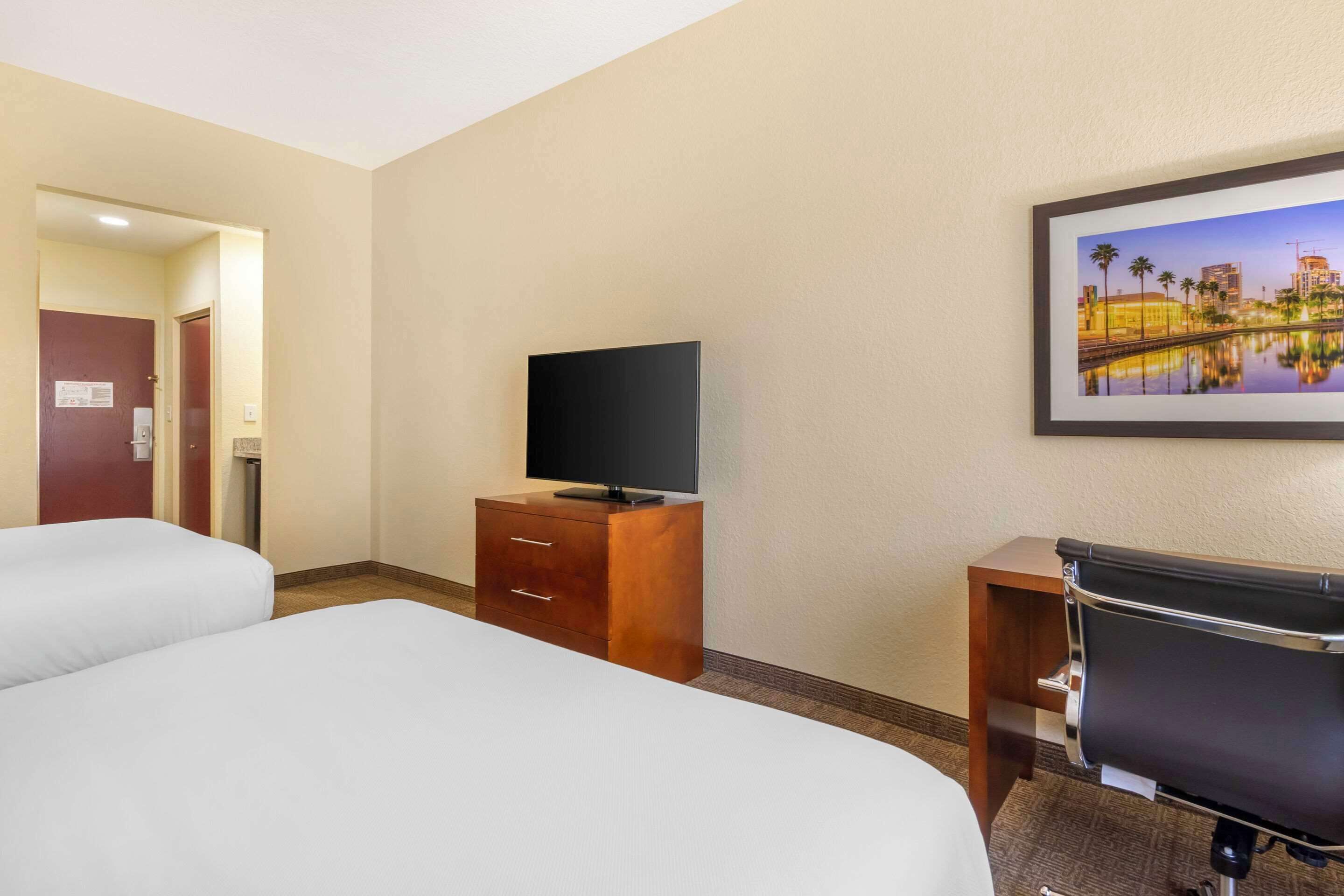 Ein Hotelzimmer mit zwei Betten, einem Fernseher auf einer Holzkommode und einem Schreibtisch mit Stuhl.