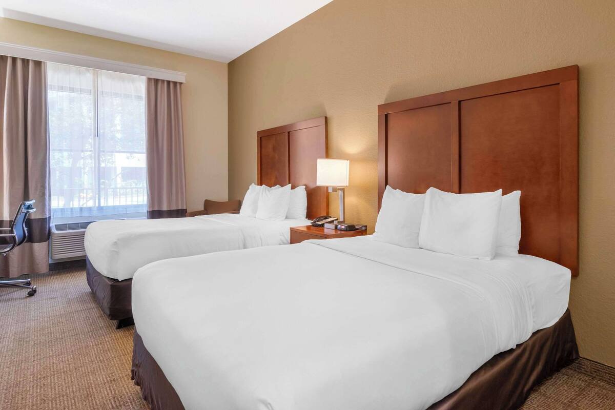 Ein Hotelzimmer mit zwei Betten, einem Schreibtisch, einem Stuhl und einem Vorhangfenster.