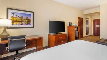 A hotel room with a bed, a desk with a chair, a television, a coffee machine, and a framed picture on the wall.