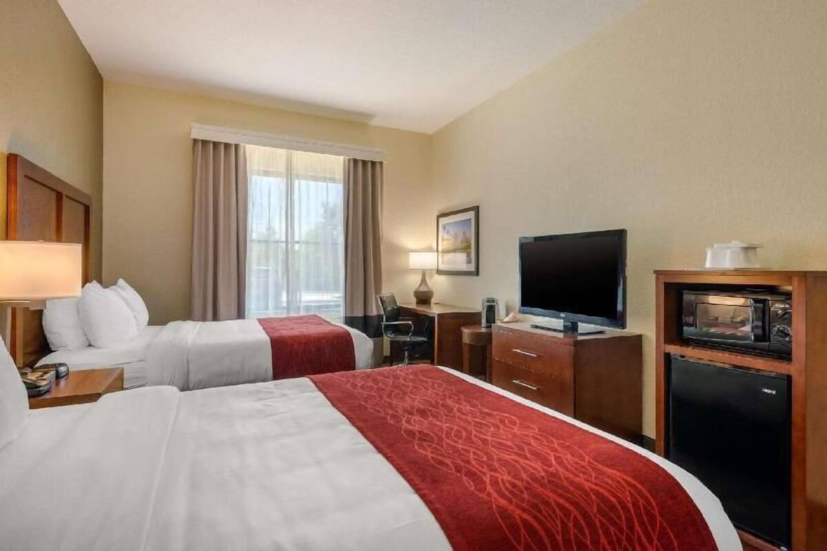 Ein Hotelzimmer mit zwei Betten, einem Schreibtisch, einem Fernseher, einer Mikrowelle und einem fenster mit Vorhängen.