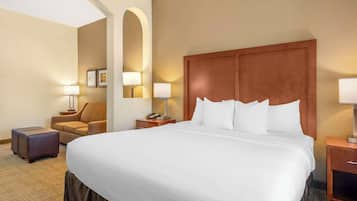 A hotel room with a large bed, a sofa, a nightstand with a lamp, and a small table with a lamp.
