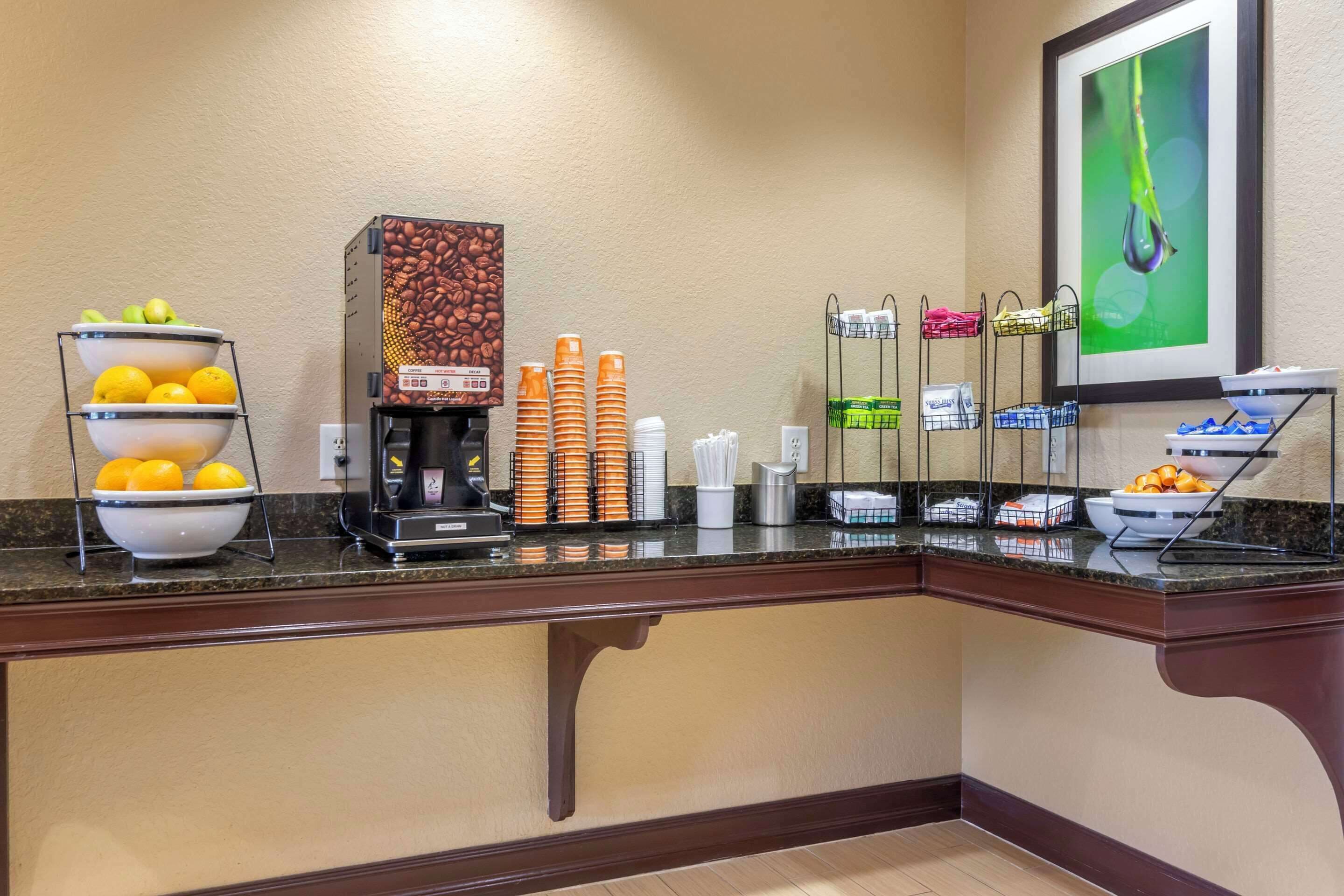 A hotel buffet area with a coffee machine, fruit bowls, and condiment dispensers.