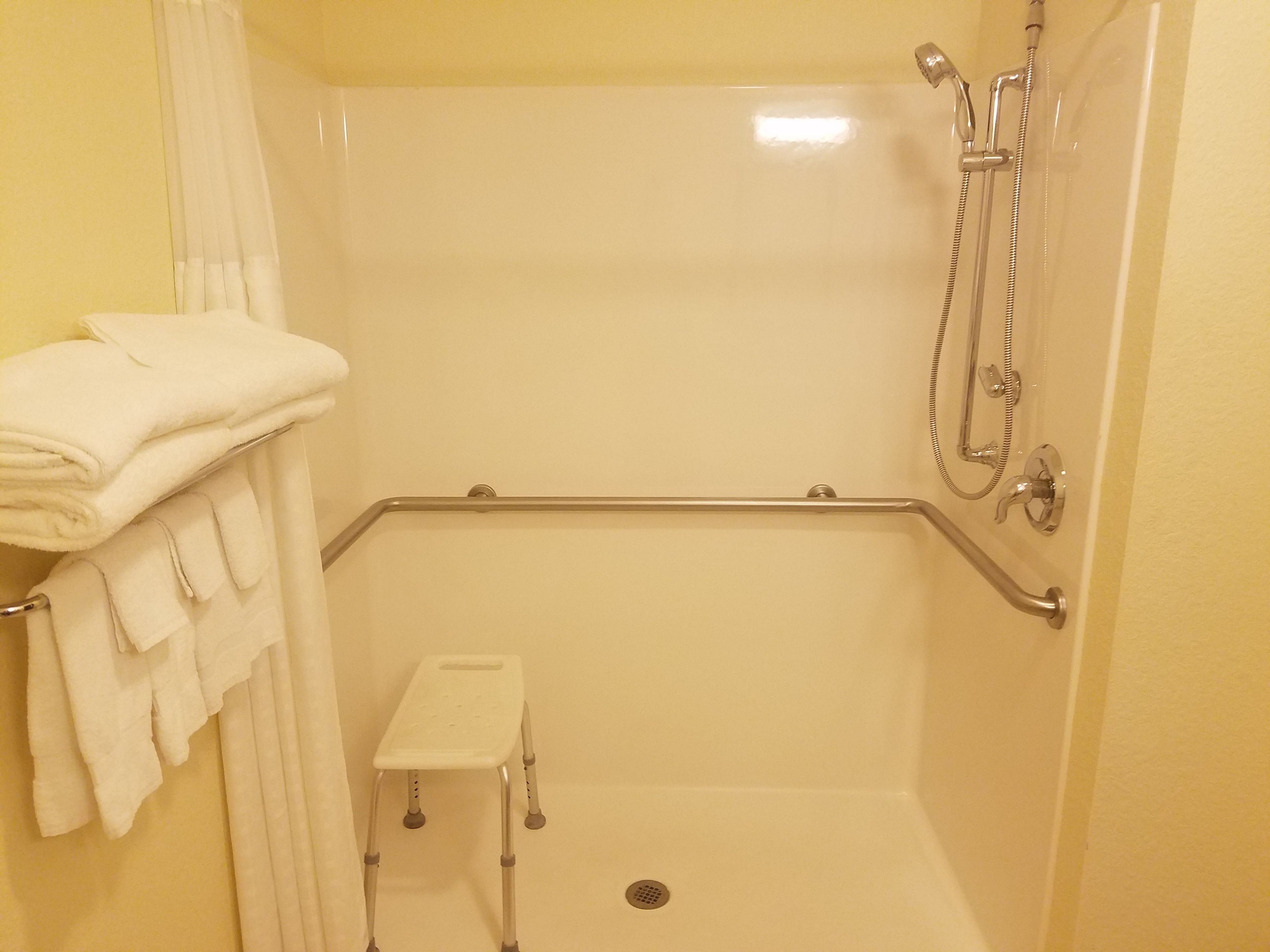 A shower area with a grab bar, a small step stool, and a towel rack with folded towels.