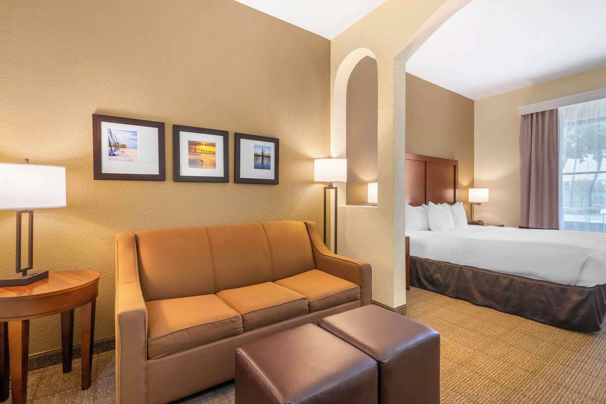 Ein Hotelzimmer mit Sofa, kleinem Tisch, Bett mit Kopfteil und gerahmten Bildern an der Wand.