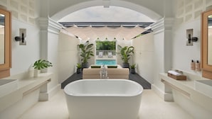 Un baño moderno con una bañera independiente, lavamanos empotrado y un amplio ventanal con vistas a una zona de piscina.