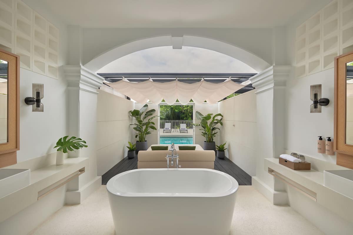 Un bany modern amb una banyera autònoma, un lavabo integrat i una finestra gran amb vista a una zona de piscina.