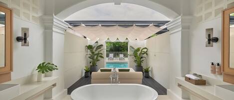 Un baño moderno con una bañera independiente, lavamanos empotrado y un amplio ventanal con vistas a una zona de piscina.