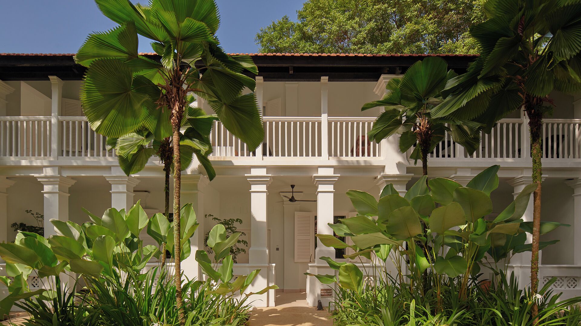 A white colonial-style building with a balcony, surrounded by tropical plants.