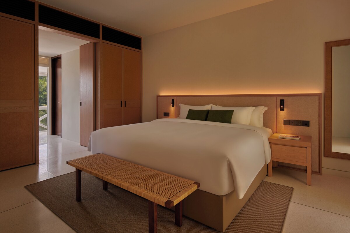 A modern bedroom with a large bed, a wooden bench, and a nightstand with a lamp.