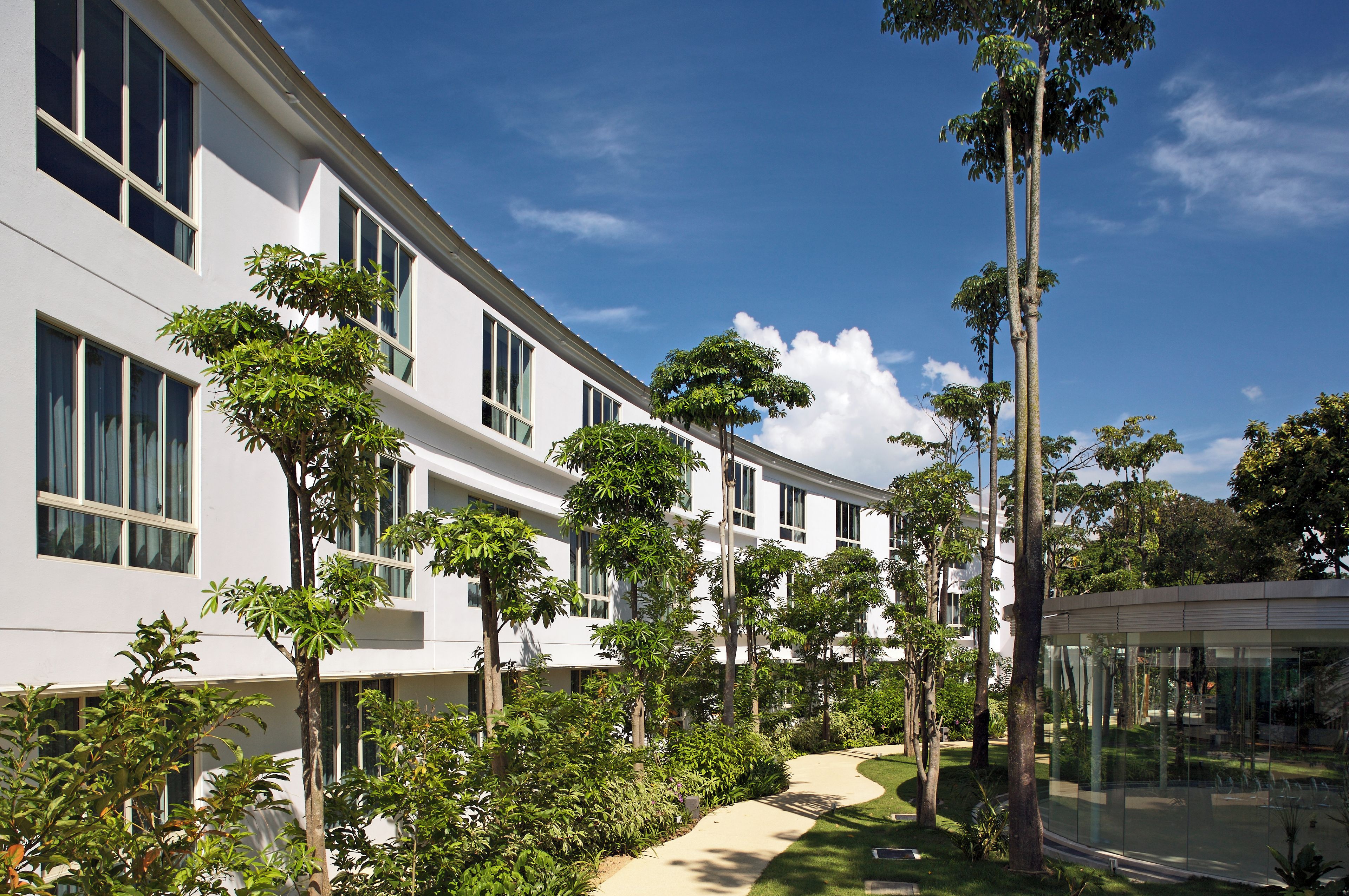A modern building with multiple windows and a pathway surrounded by greenery.