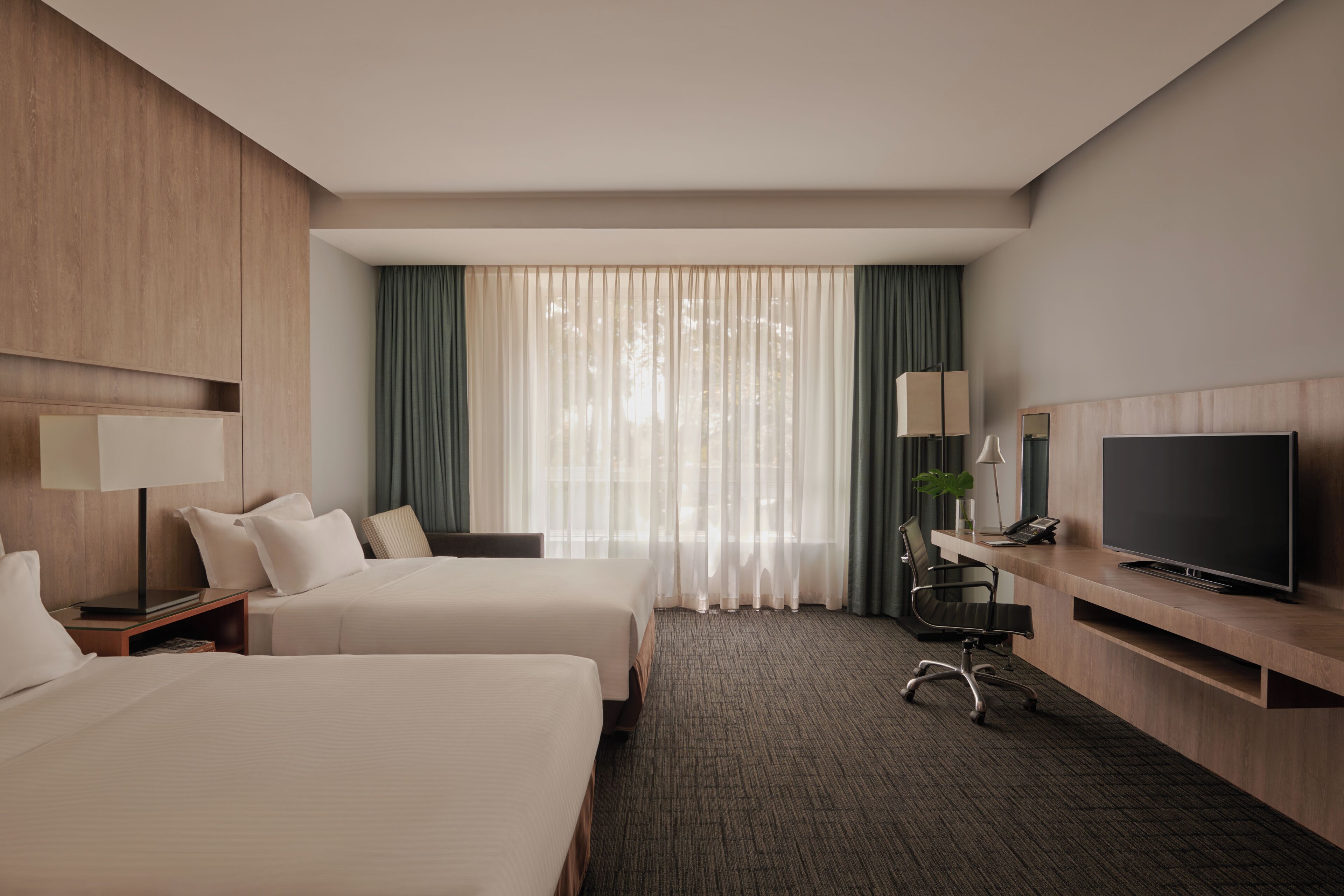 A hotel room with two beds, a desk with a TV, a lamp, and a chair.