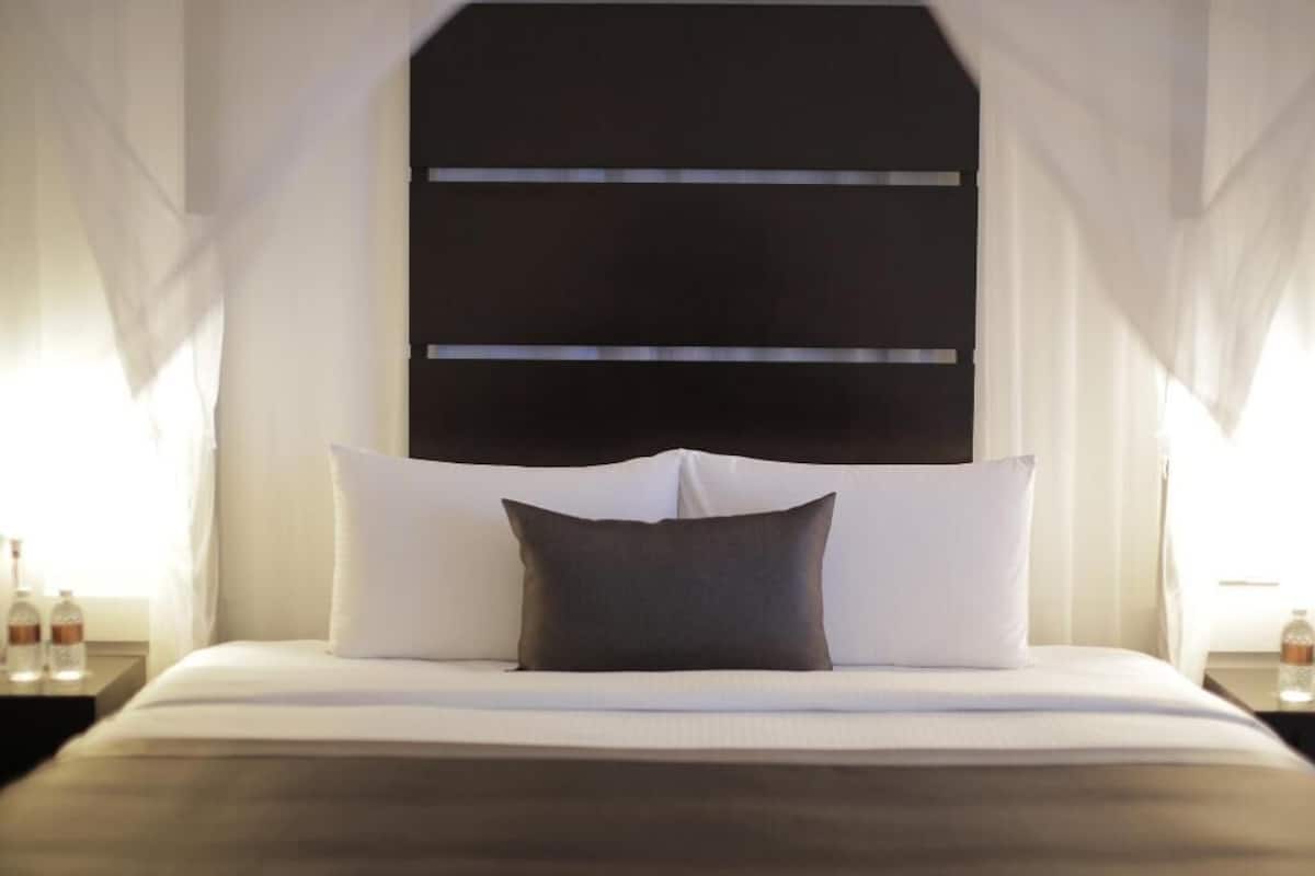 Habitació d'hotel amb llit, cortines blanques i capçal de llit negre.