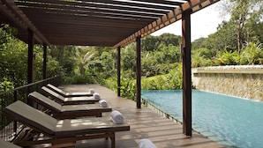 Una terraza de madera con sillones de descanso y una piscina.
