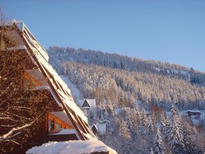 Una cabaña de madera con techo inclinado, rodeada de árboles cubiertos de nieve y un cielo azul despejado.
