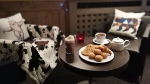 Un cuarto acogedor con una cama, una mesita con galletas y croissants, una taza de té y un vaso de chocolate caliente.
