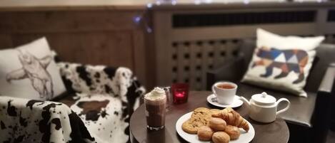 A cozy room with a bed, a small table with a plate of cookies and croissants, a cup of tea, and a glass of hot chocolate.