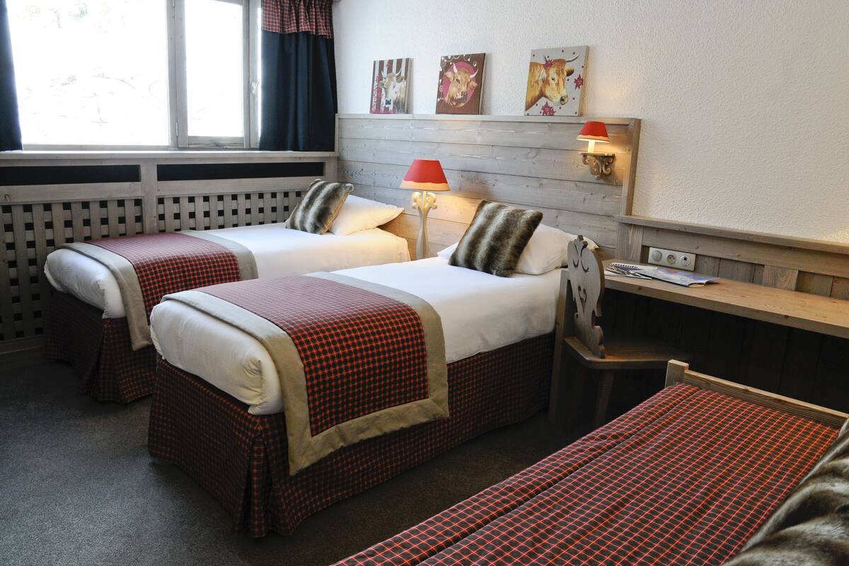 Une chambre d’hôtel avec deux lits, un bureau et un banc. Les murs sont ornés de lampes et de tableaux représentant des animaux.