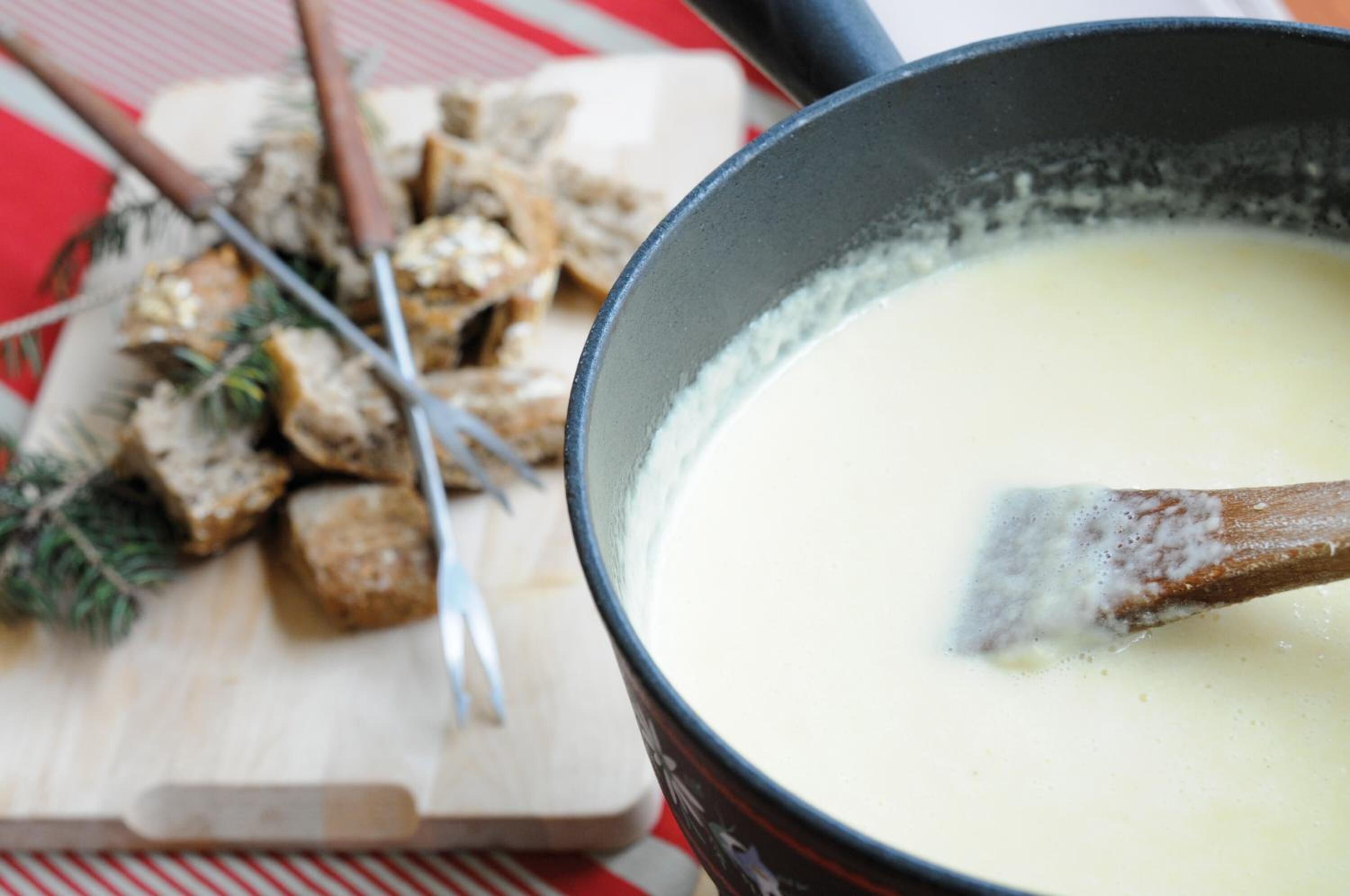 A pot of soup with a wooden spoon, a cutting board with cubed food, and a red and white striped cloth.