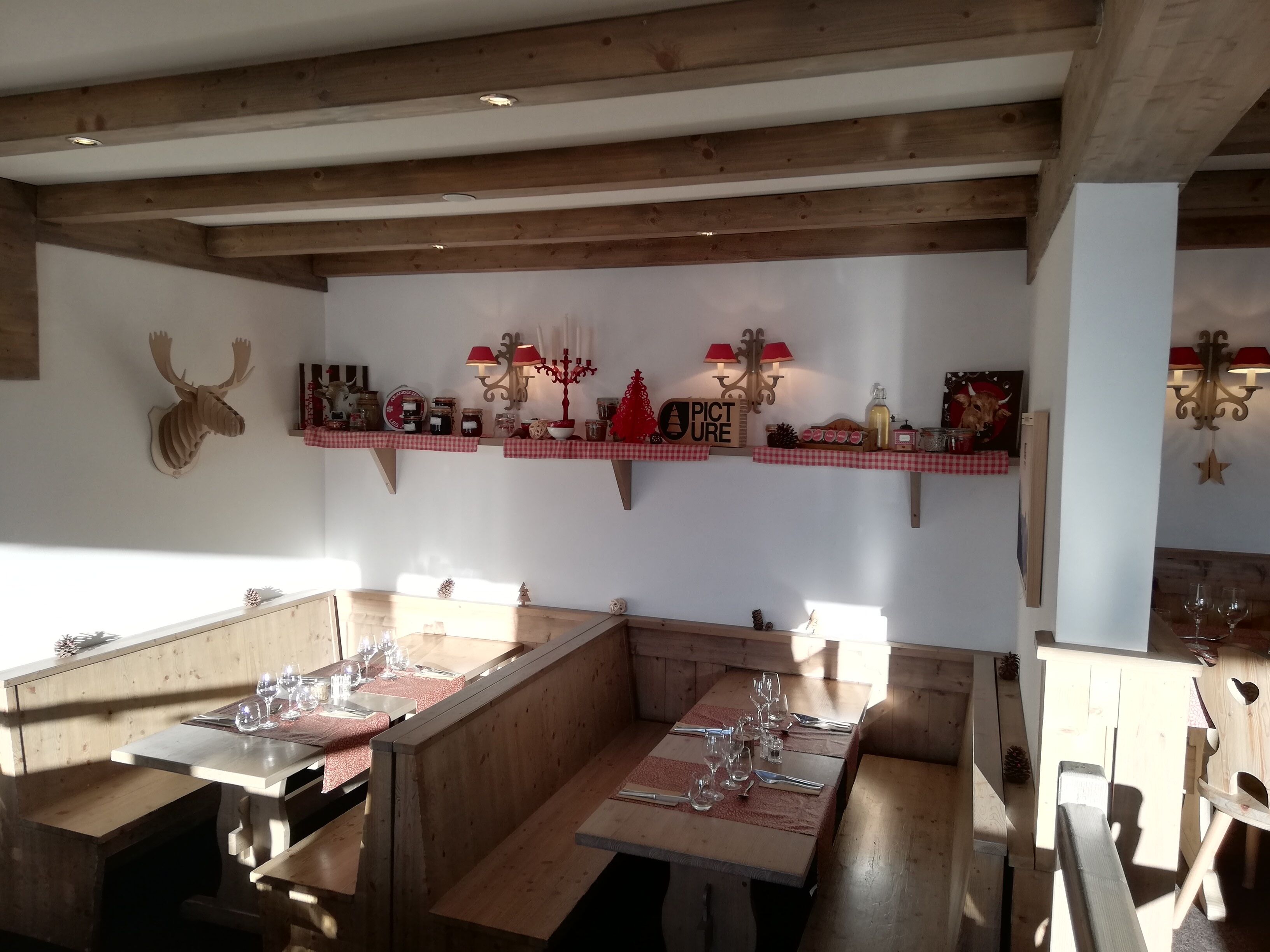 Un restaurant chaleureux avec des poutres en bois, des nappes à carreaux rouges et blancs, et une variété de décorations, notamment une tête d’élan, une enseigne avec l’inscription « Photo » et des lampes fixées au mur.