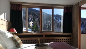 Un dormitorio con cama, ventana con vista a una montaña nevada, lámpara roja y planta en maceta.