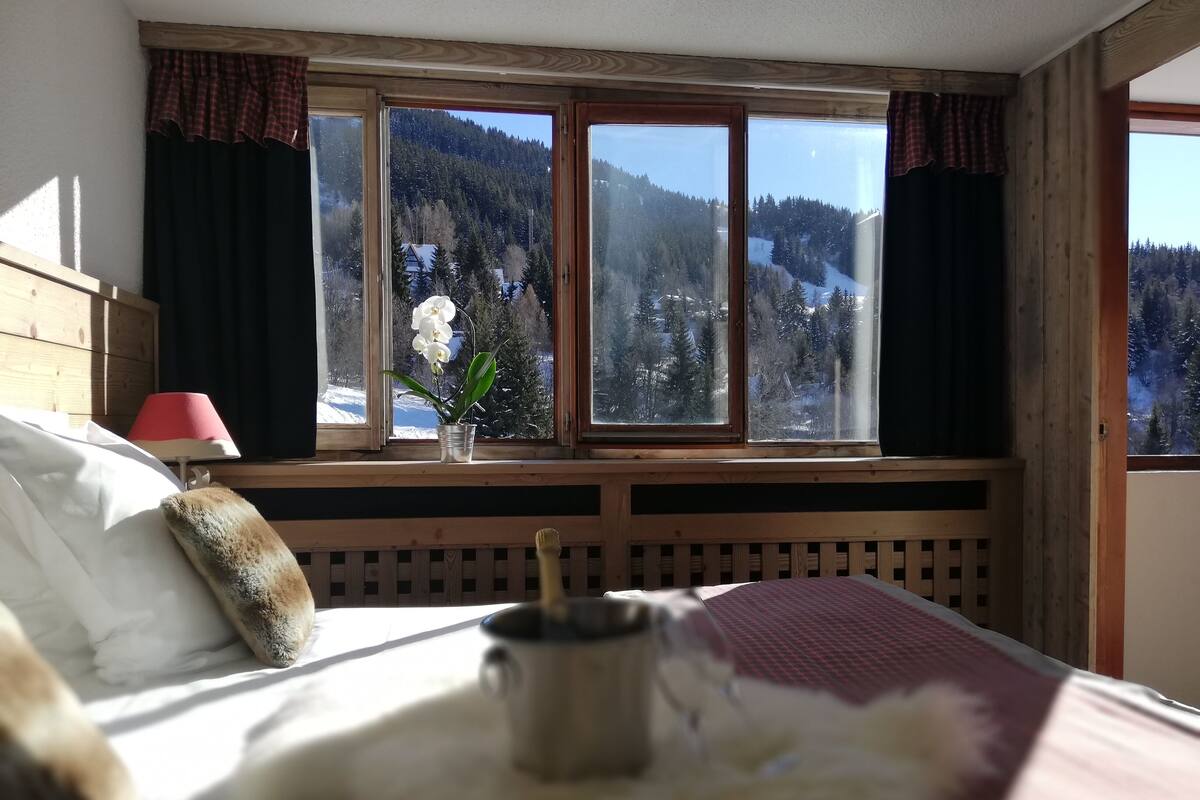 Une chambre à coucher avec un lit, une fenêtre donnant sur une montagne enneigée, une lampe rouge et une plante en pot.