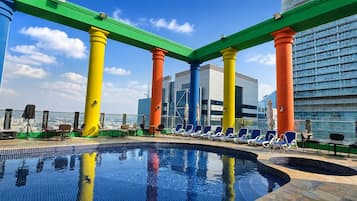 A rooftop pool area with a clear view of the city skyline, surrounded by colorful columns and lounge chairs.