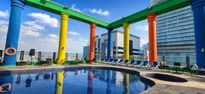 A rooftop pool area with a clear view of the city skyline, surrounded by colorful columns and lounge chairs. - Oryx Hotel (Abu Dhabi)