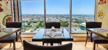 Un comedor con una mesa dispuesta para dos personas, ventanas amplias con vista a la ciudad y una pared decorada con un mural alusivo a los tacos.
