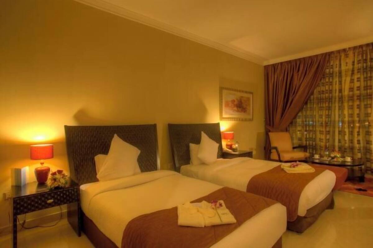 A hotel room with two beds, a nightstand with a lamp, a chair, and a small table with a tray.